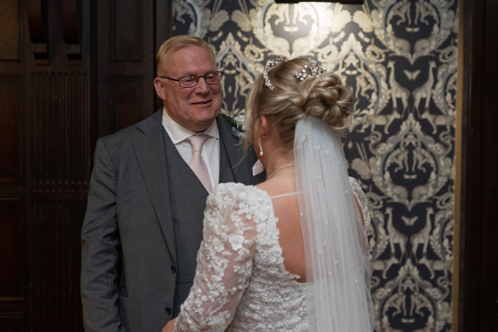 A father seeing his daughter in her wedding dress for the first time, smiling and welling up behind his glasses