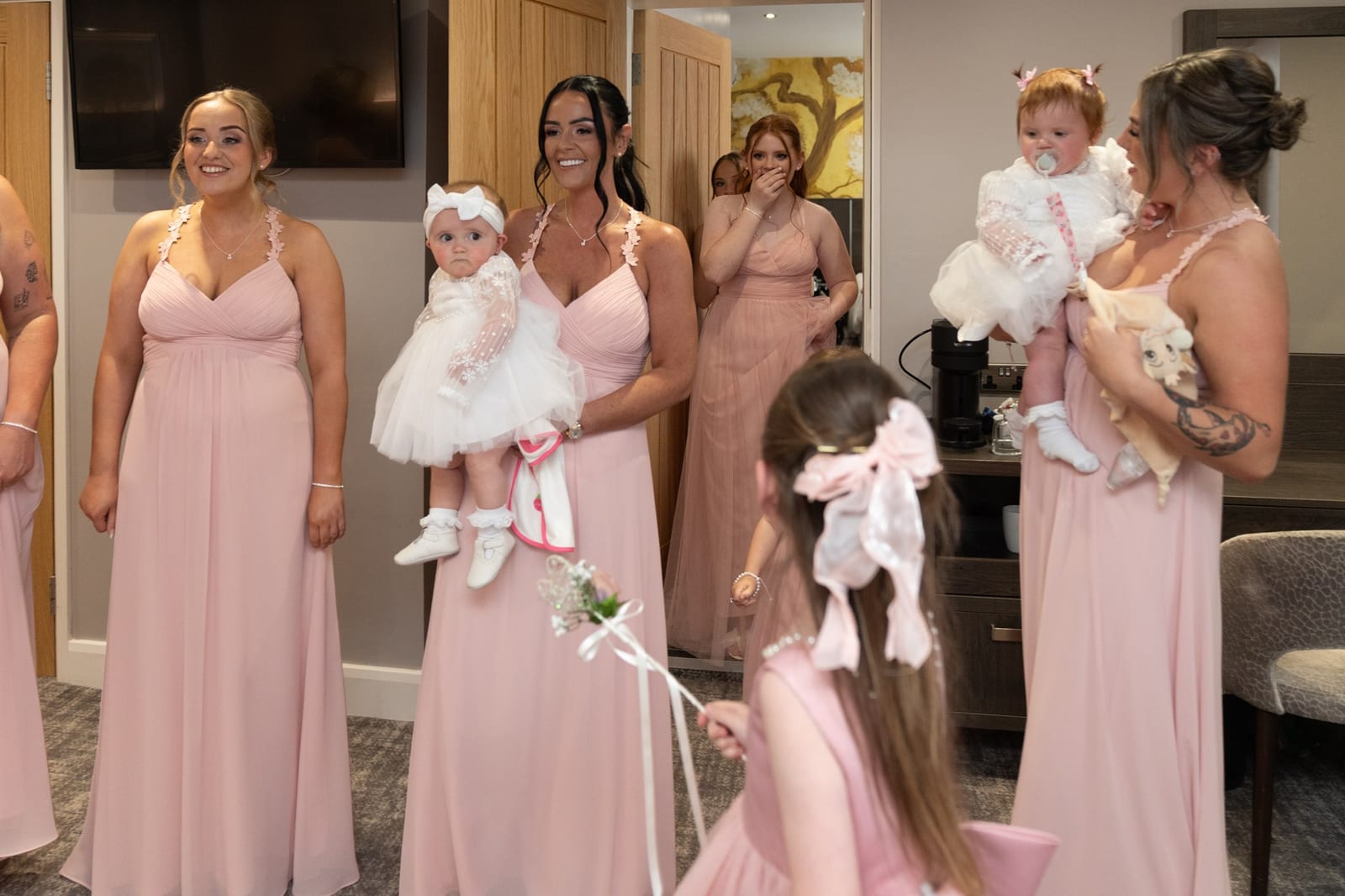 Bridesmaids in pink seeing the dress for the first time — one covering her mouth, a flower girl watching with her wand