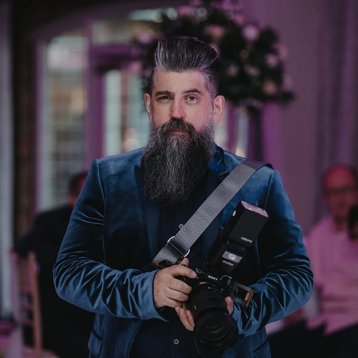 Wayne, The Bearded Wedding Photographer, camera in hand mid-wedding in a blue velvet jacket