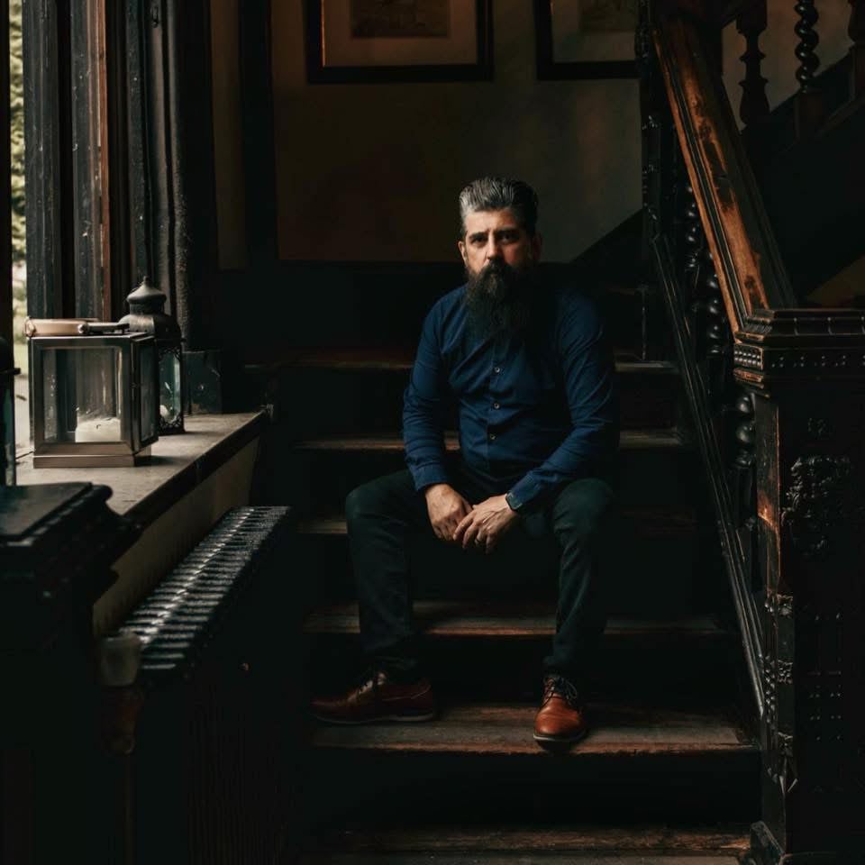 Wayne, The Bearded Wedding Photographer, sitting on a dark wooden staircase in low light