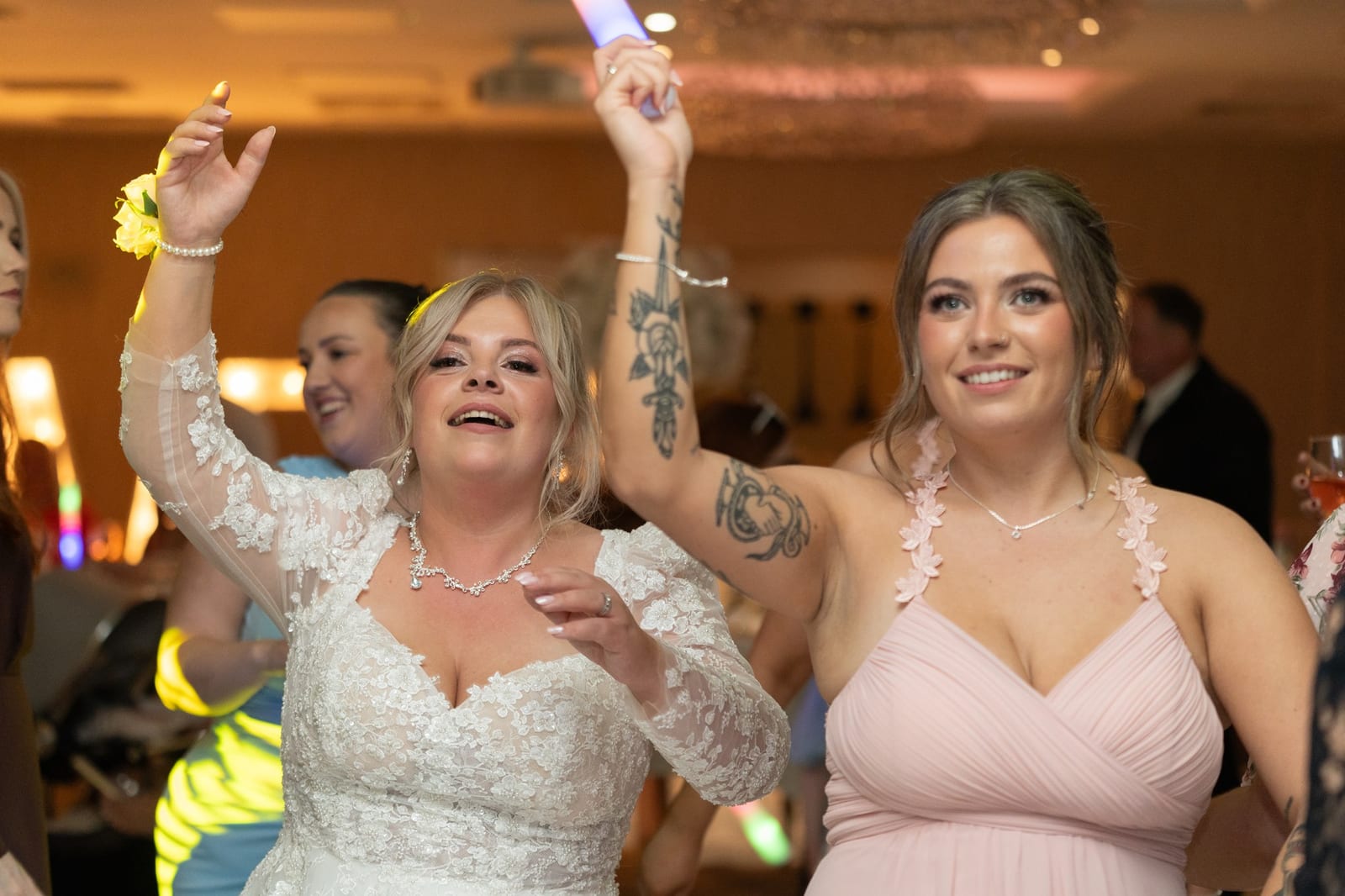 The bride mid-dance with arms raised beside a bridesmaid, both singing, completely unaware of the camera
