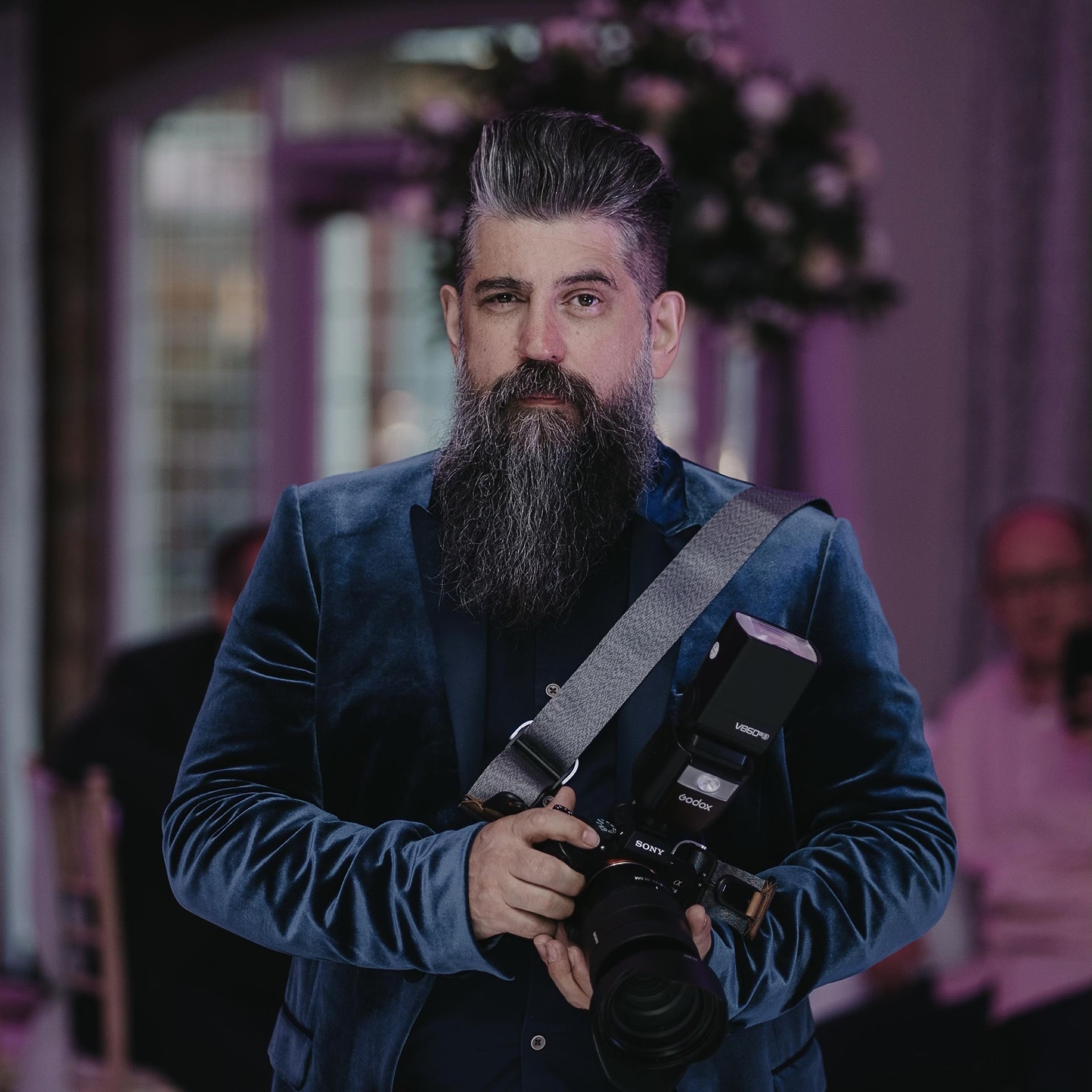 Wayne Myers — The Bearded Wedding Photographer, holding his camera at a wedding reception