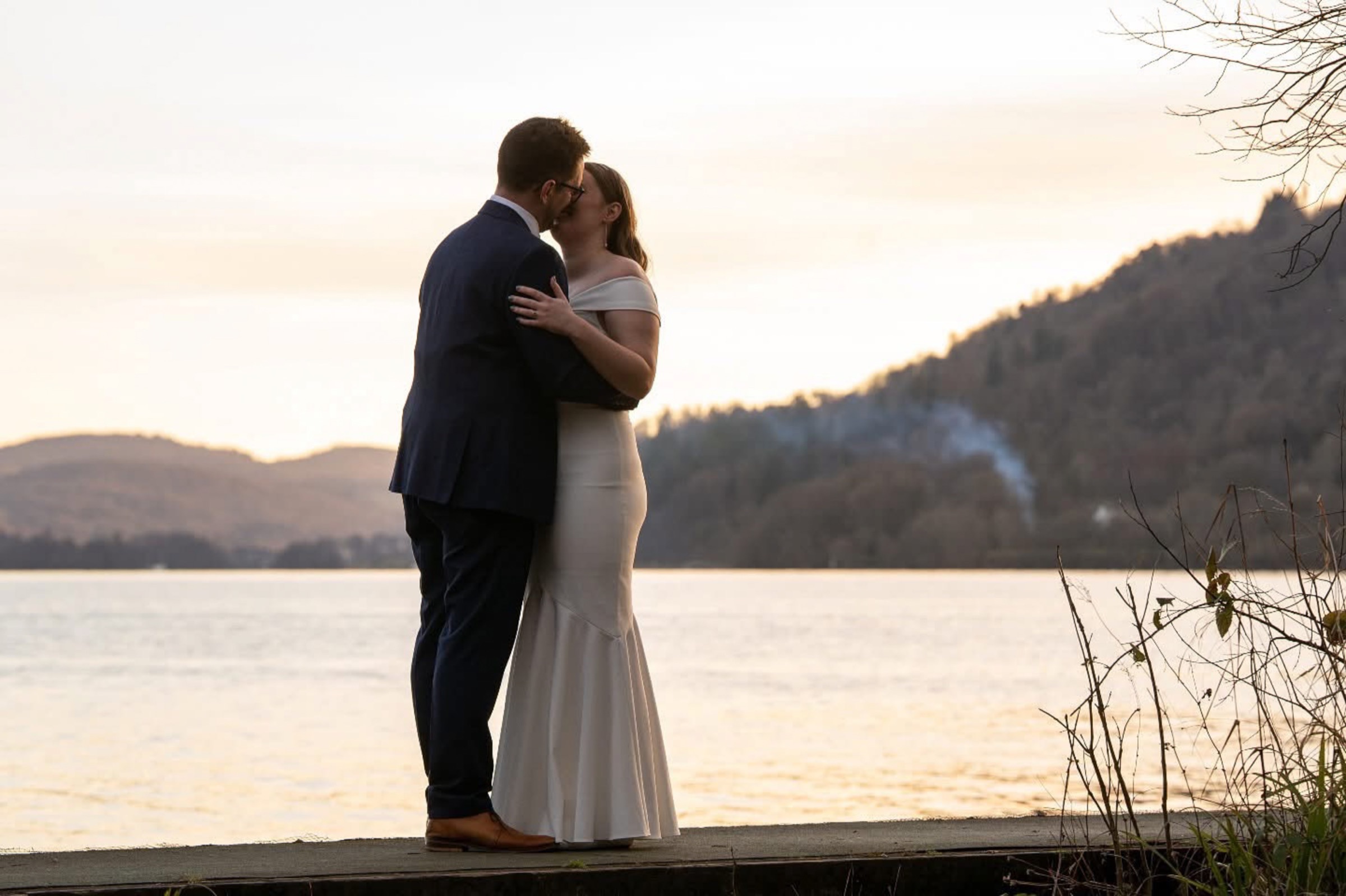 A couple share a quiet kiss on a wooden jetty as dusk settles over a Lake District lake