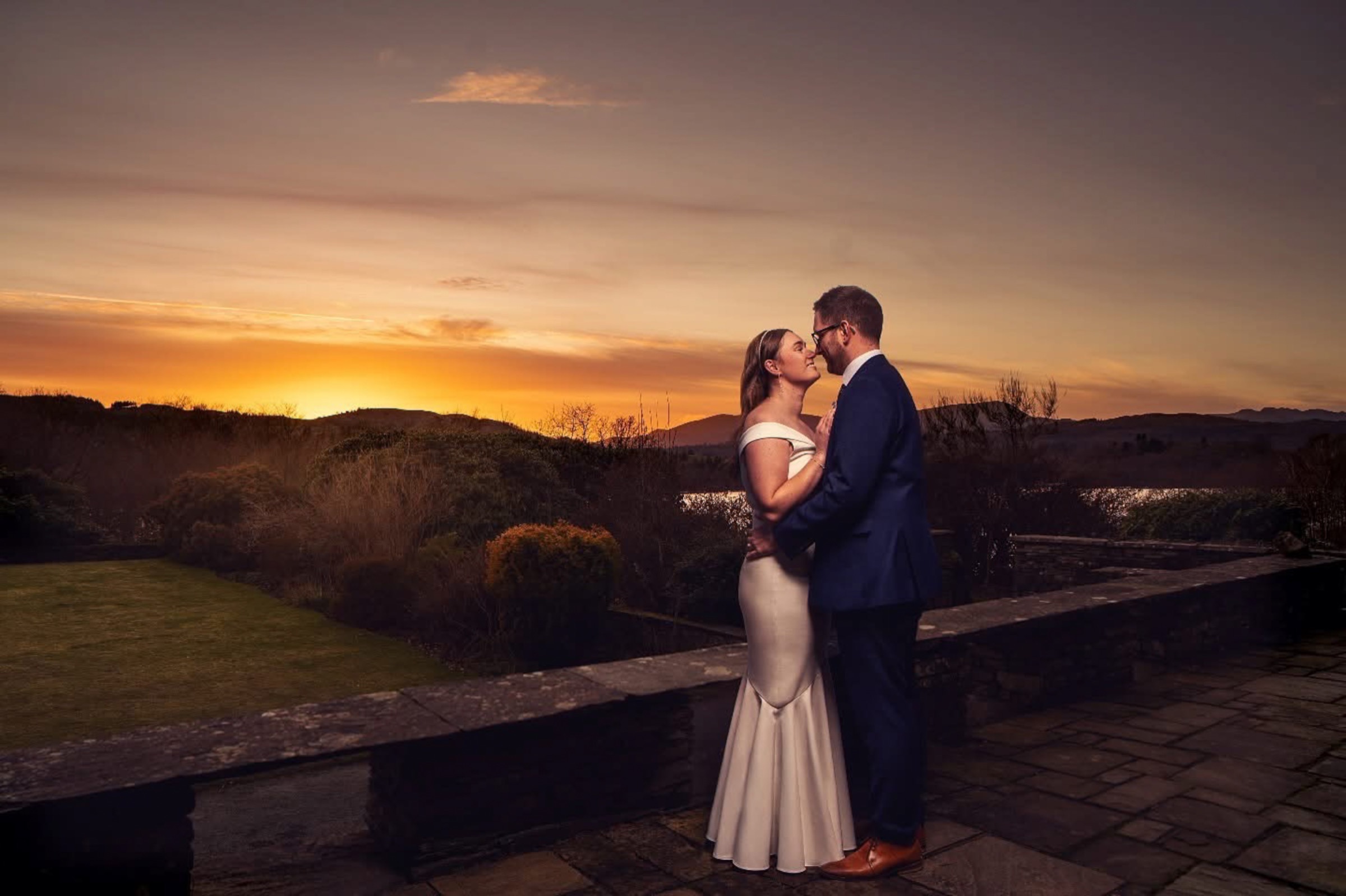 Couple embracing on a stone terrace against a dramatic orange sunset