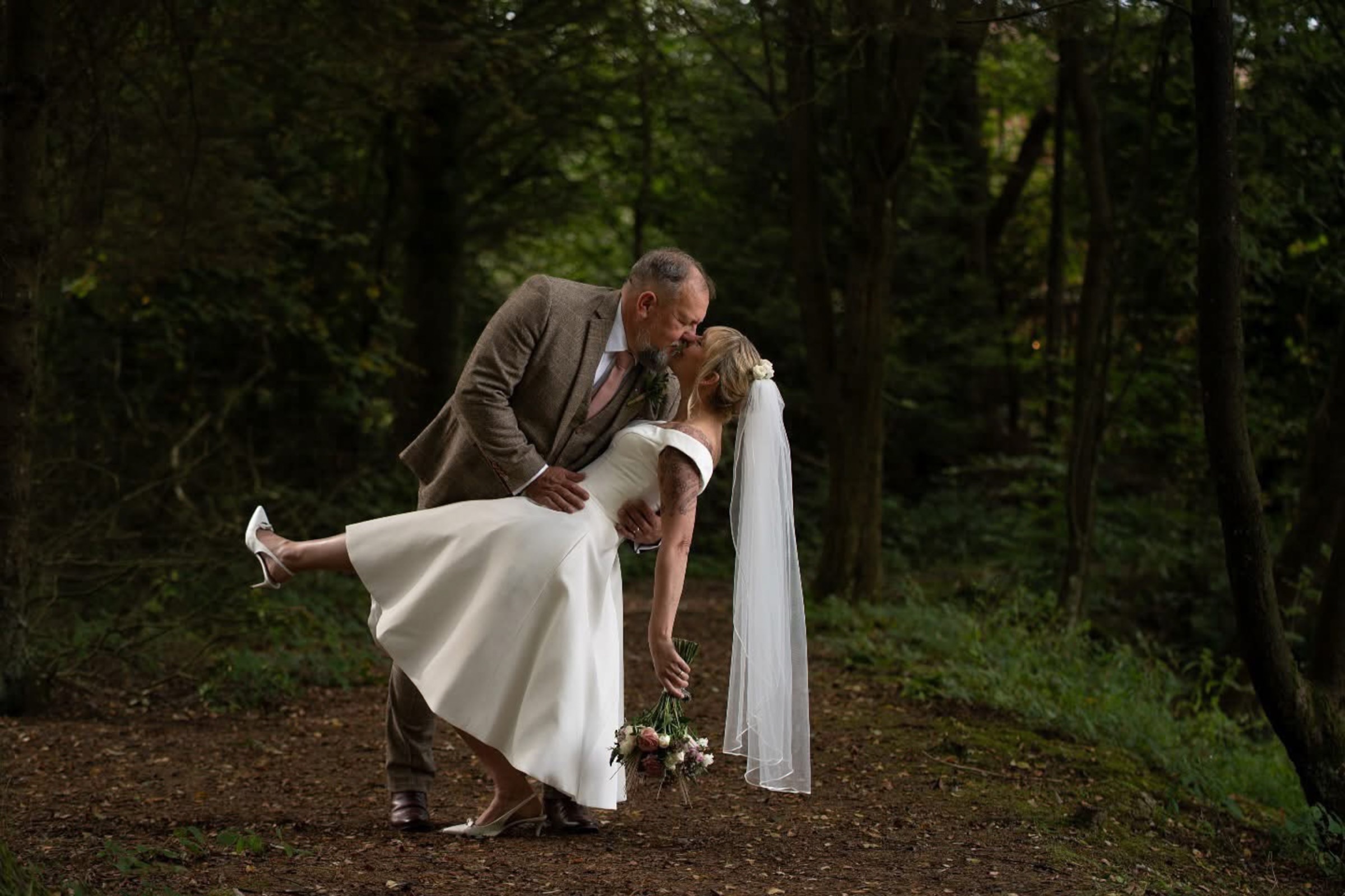 A groom dips his bride in a woodland clearing — the full sweep of the moment, uncropped