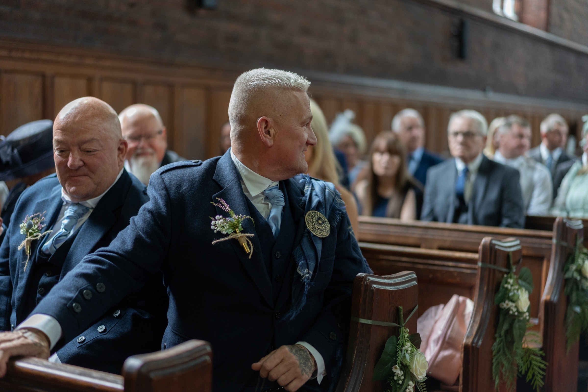 The groom sits in a church pew looking back over his shoulder — nervous, expectant