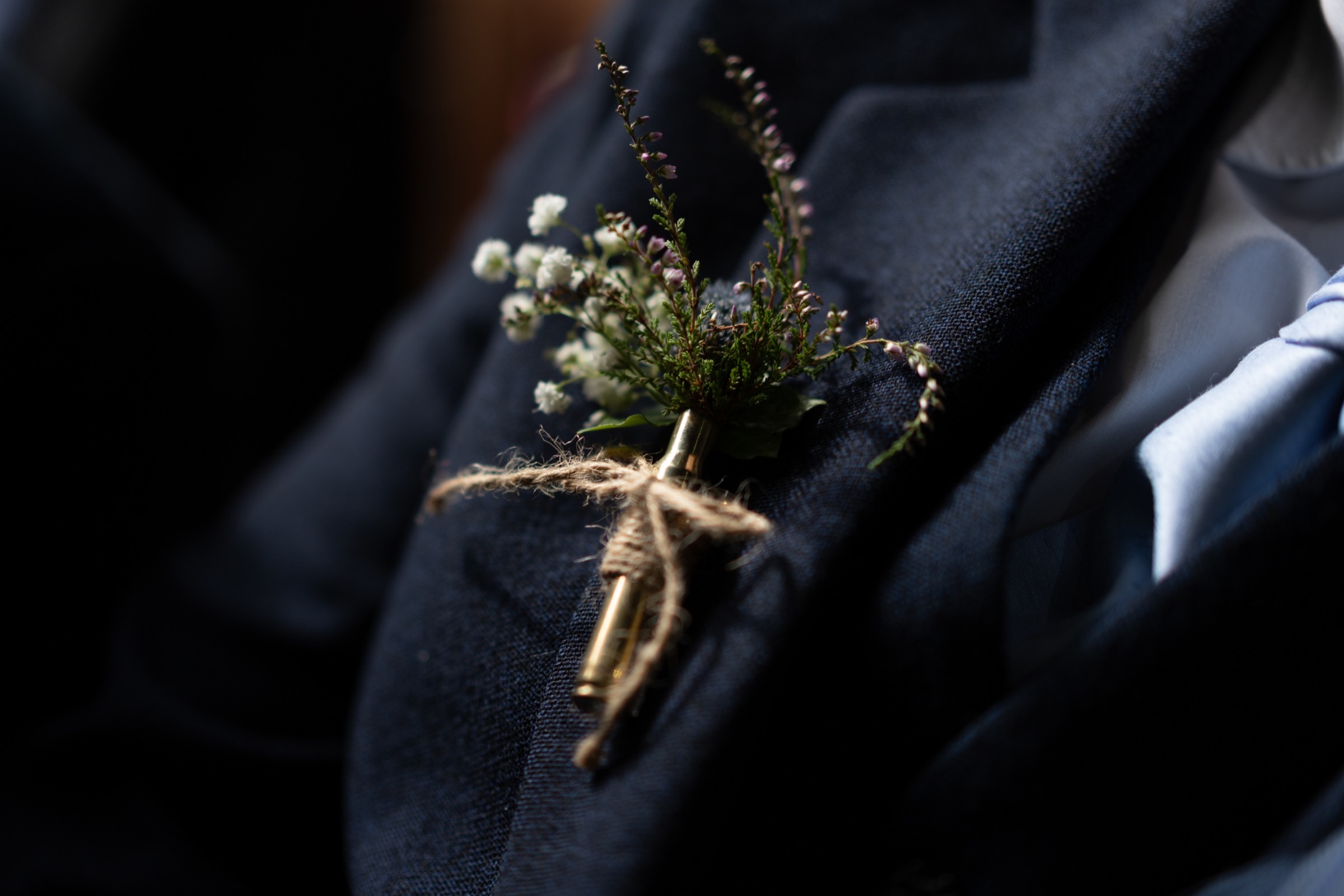 A close-up of a boutonnière — heather and wildflowers tied with twine to a dark jacket lapel