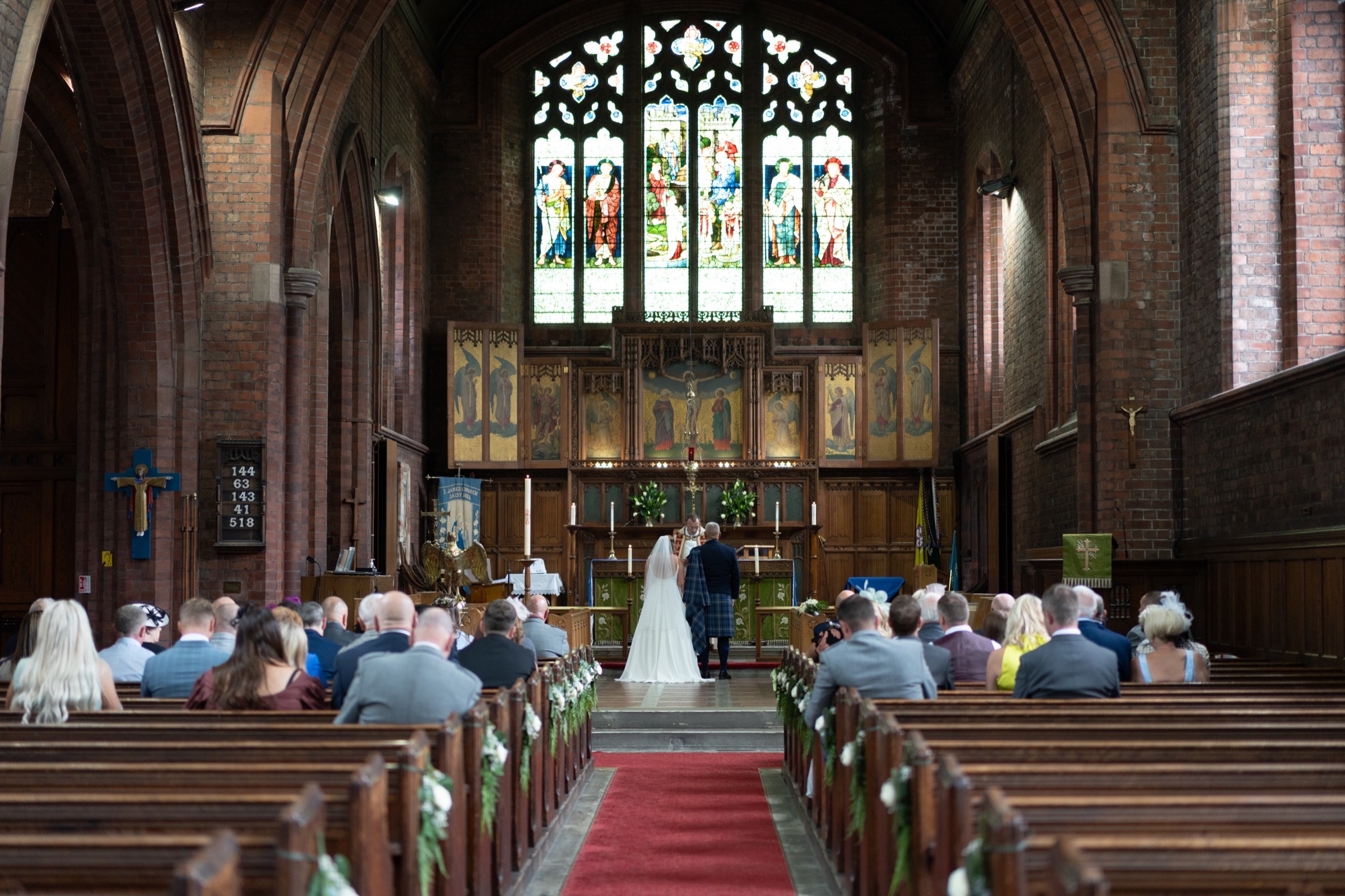 A couple stand at the altar — stained glass behind them, guests filling the pews on either side